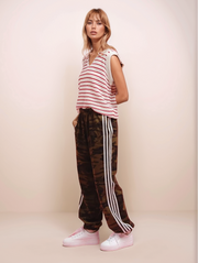 Woman wearing a striped shirt and camouflage pants with white stripes on a beige background