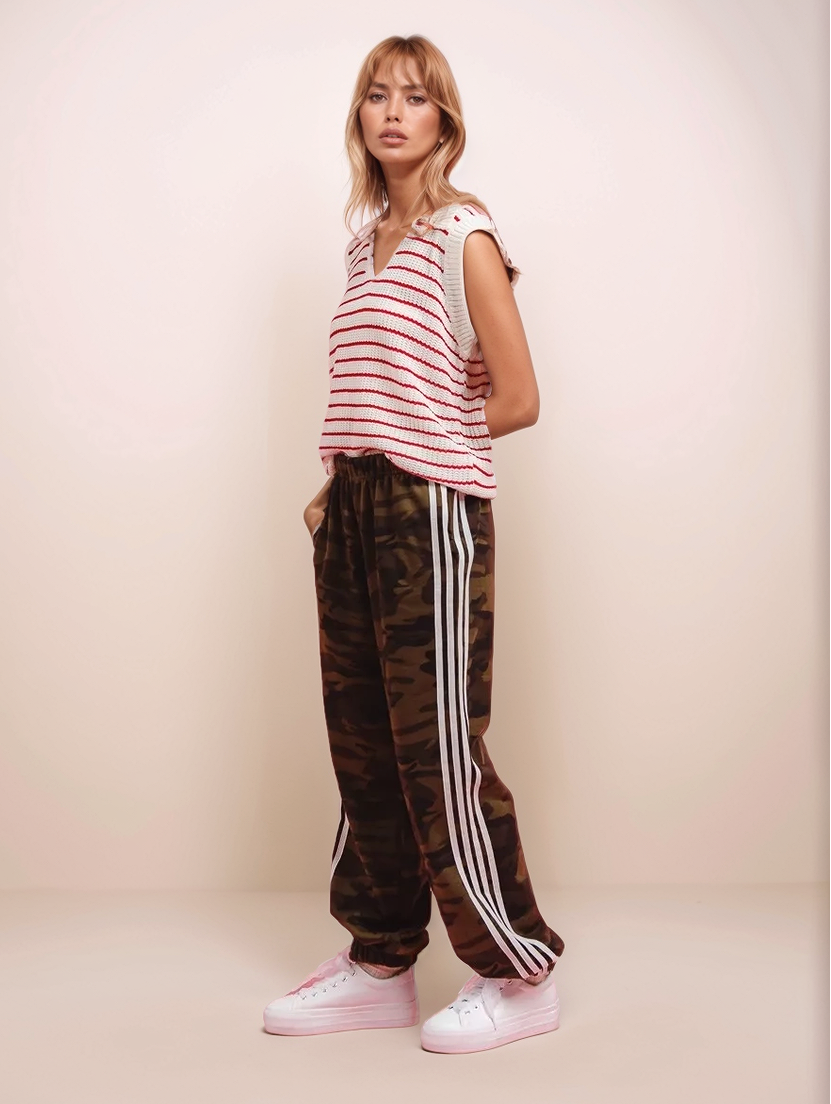 Woman wearing a striped shirt and camouflage pants with white stripes on a beige background
