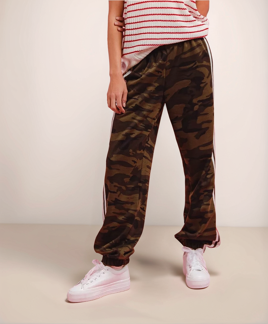 Person wearing camouflage jogger pants and pink sneakers on a beige background