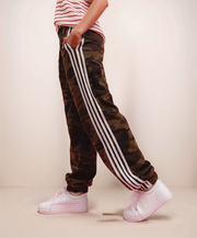 Camouflage jogger pants with three white stripes worn by a person on a beige background