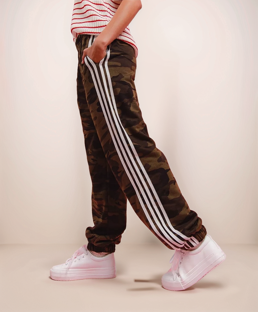 Camouflage jogger pants with three white stripes worn by a person on a beige background