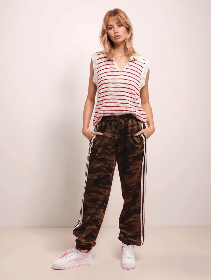 Woman wearing a striped sleeveless top and camouflage pants with white stripes on a plain background
