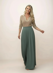 Woman wearing a beige top and green skirt on a plain background