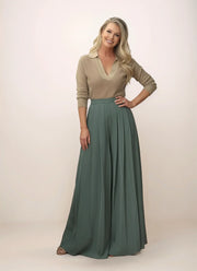 Woman wearing a beige top and green wide-leg pants on a plain background