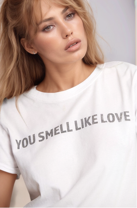 Woman wearing a white t-shirt with text 'YOU SMELL LIKE LOVE' against a neutral background